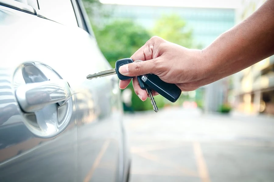 Driver holding a car key beside a vehicle door handle.