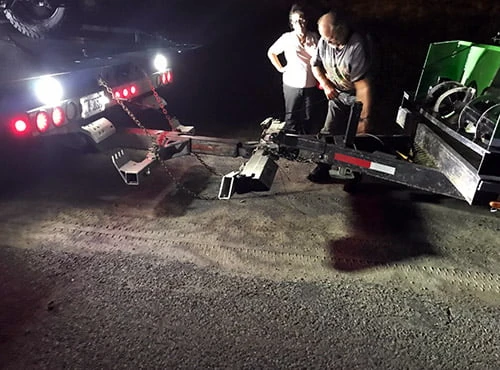 Tow operator handling recovery equipment beside a flatbed at night.