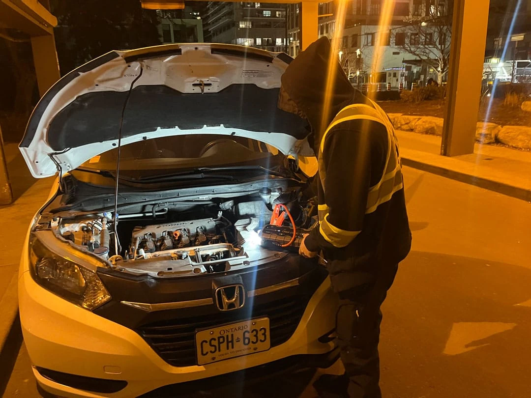 Technician working under the hood of a Honda during nighttime battery assistance.