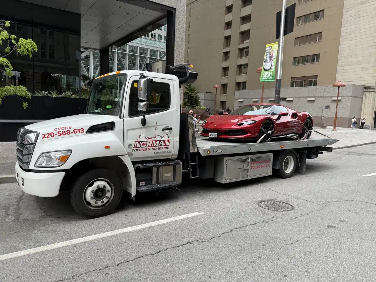 Red sports car secured on a Norman Towing flatbed beside a building.