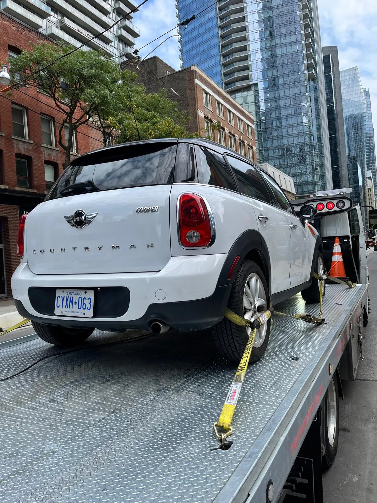 White Mini secured on a flatbed in a city street.