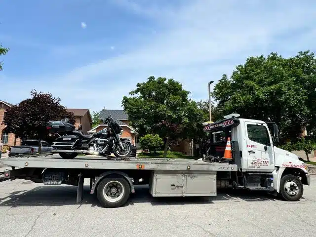 Motorcycle secured on a Norman Towing flatbed on a residential street.