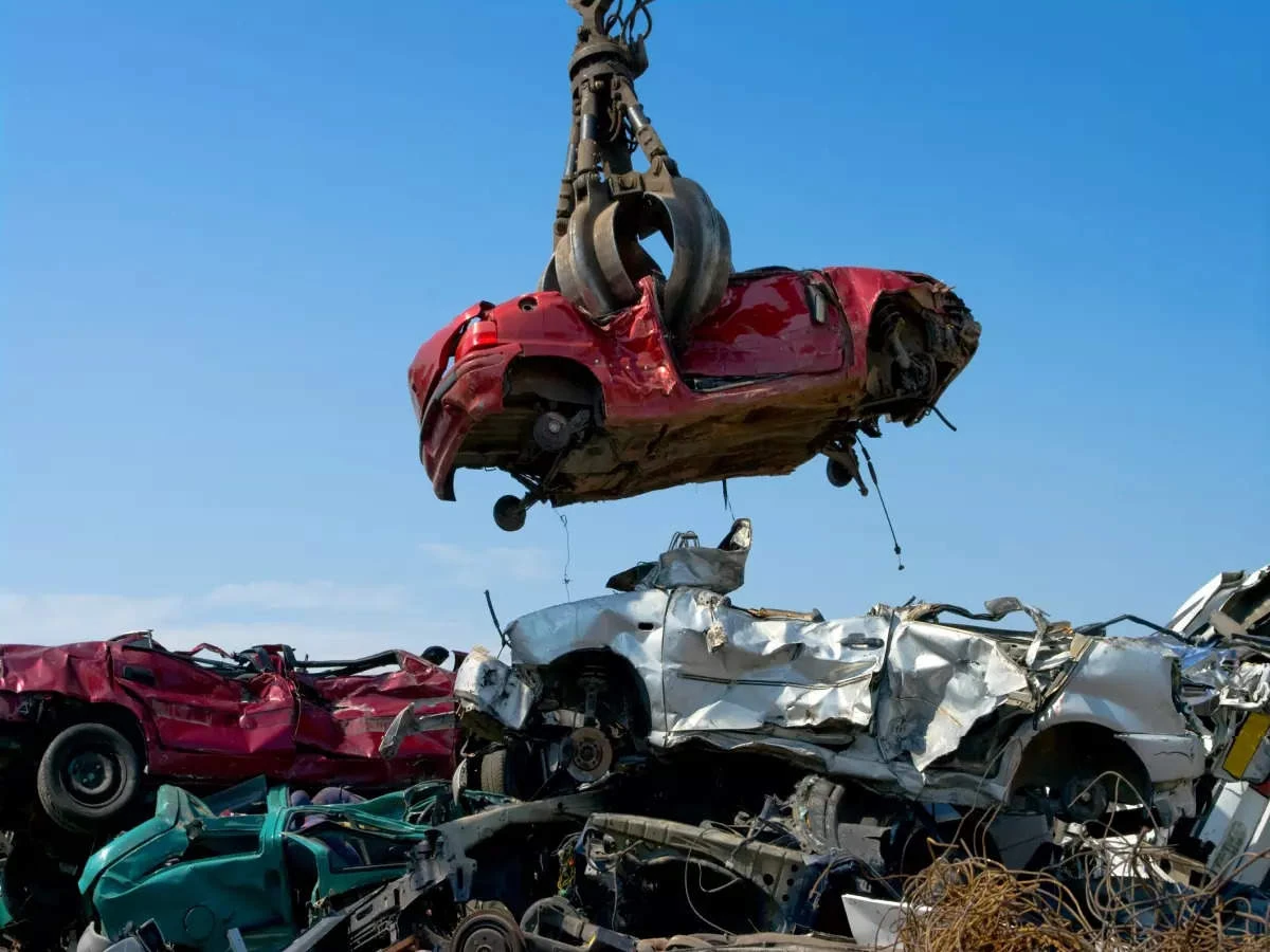 Crane lifting a crushed car at a vehicle recycling yard.