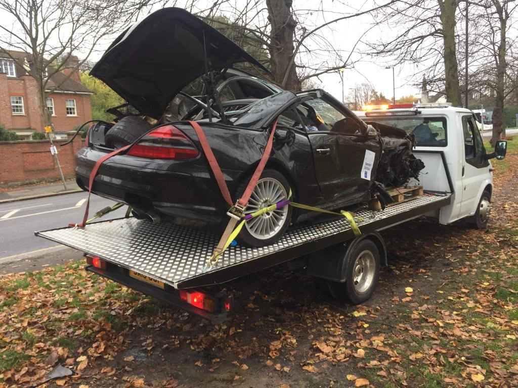 Severely damaged car secured with straps on a flatbed truck.