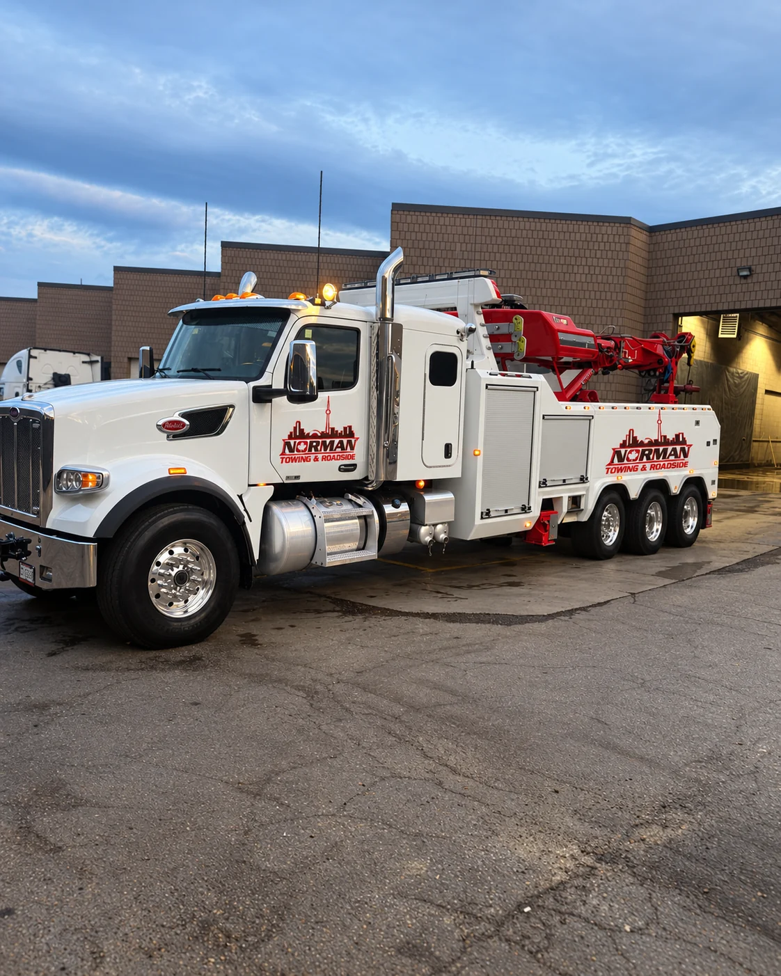Heavy Duty Tow Truck Service | Norman Towing Norman Towing heavy duty tow truck with white body and red equipment parked outside an industrial building.