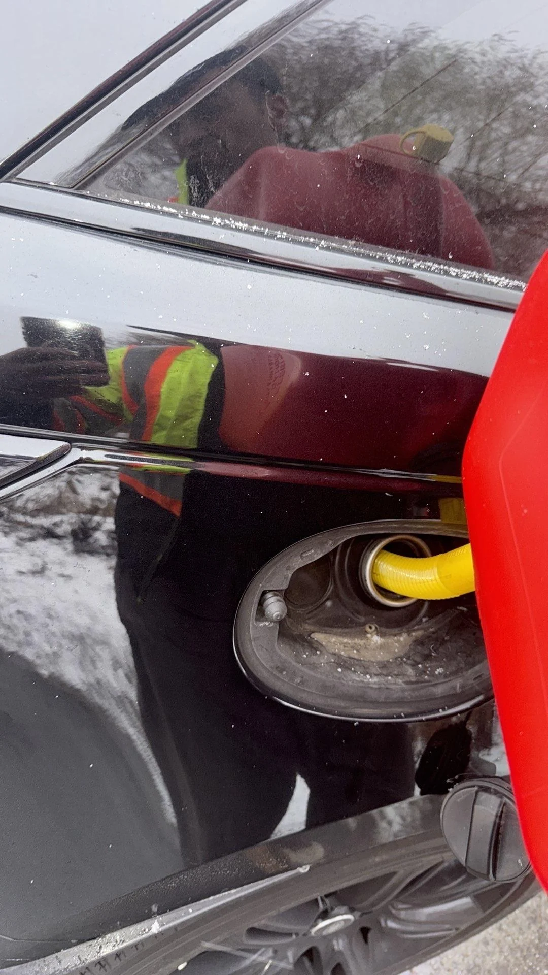 Roadside Fuel Delivery Service | Norman Towing Yellow fuel nozzle inserted into a black vehicle during winter roadside fuel delivery.