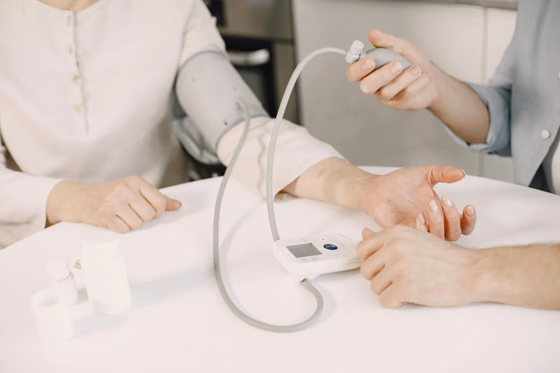 Person wearing a blood pressure cuff on the arm having blood pressure measured with a digital monitor by another individual.