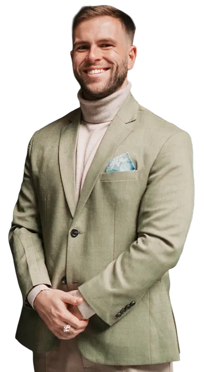 Smiling man in a light green blazer and beige turtleneck posing with hands clasped.