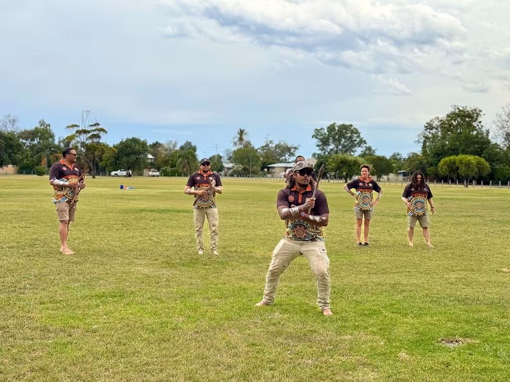Group of five Walaaybaa Rangers standing on grass field, holding decorated shields and traditional weapons outdoors.