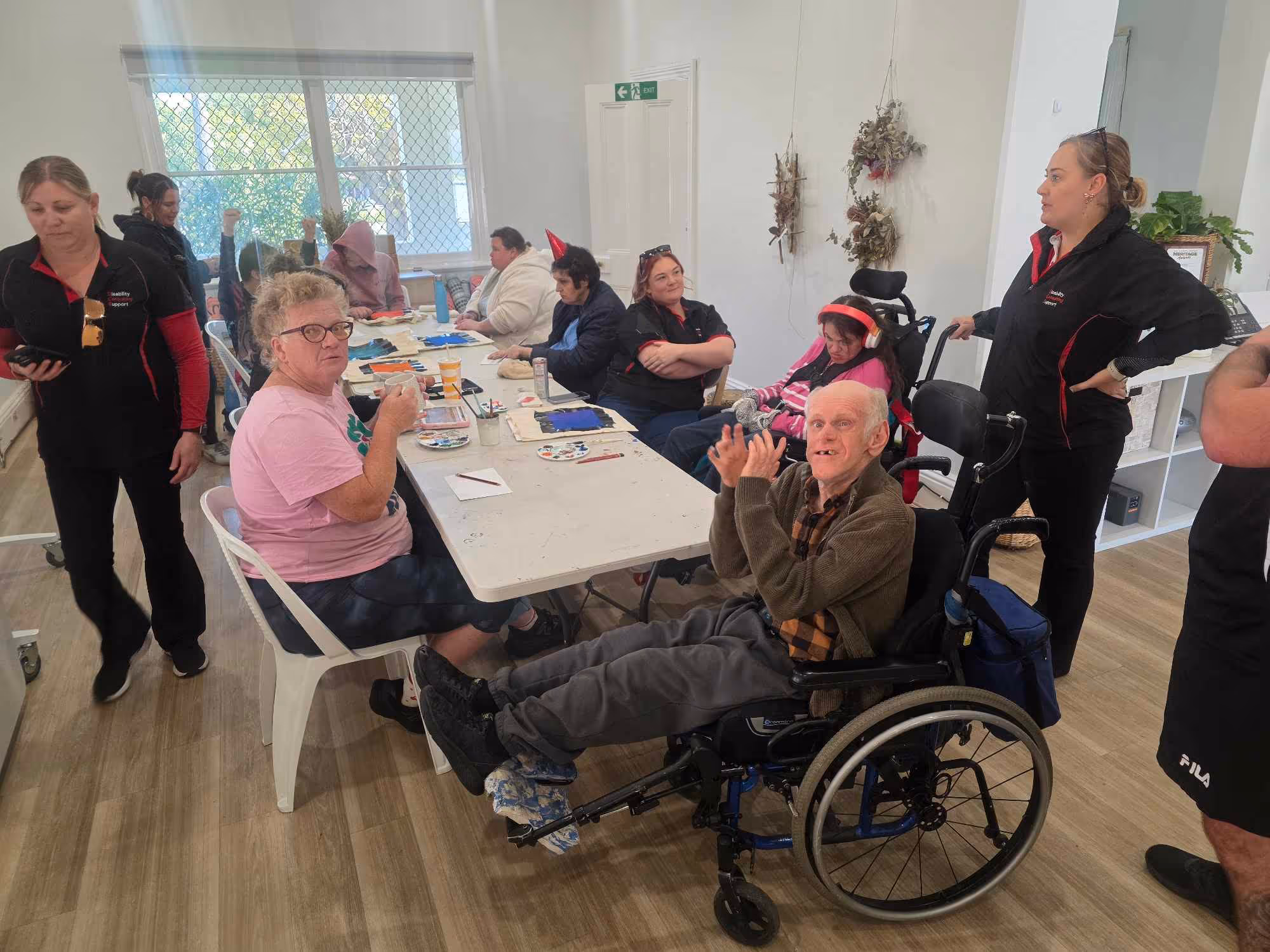 Group of people with disabilities and caregivers around a table in a bright room doing activities.