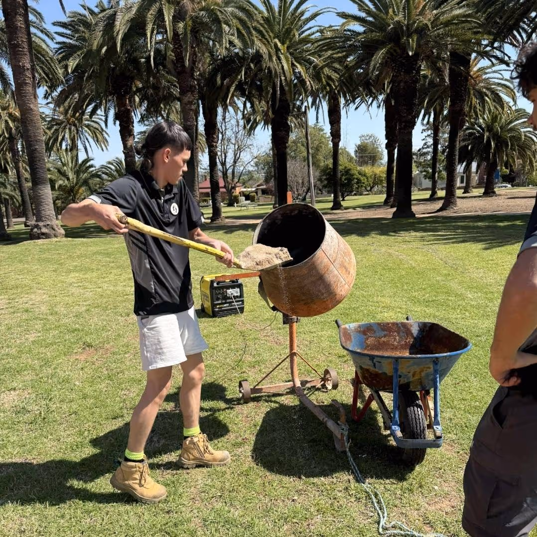 A Fresh footprints participant shovels materials into a standing cement mixer