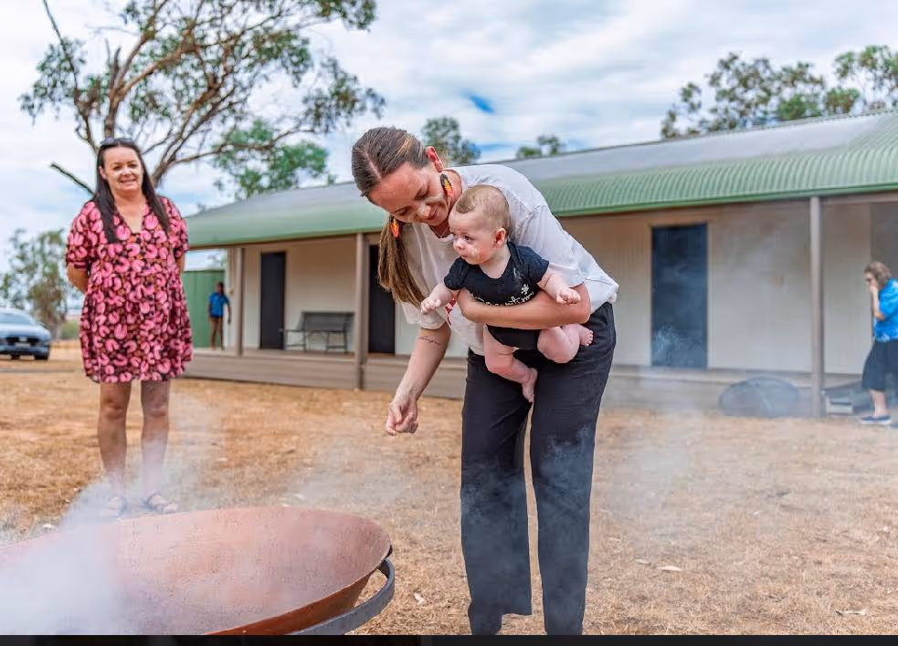 A mother holds her infant near ceremonial smoke as part of a smoking ceremony.