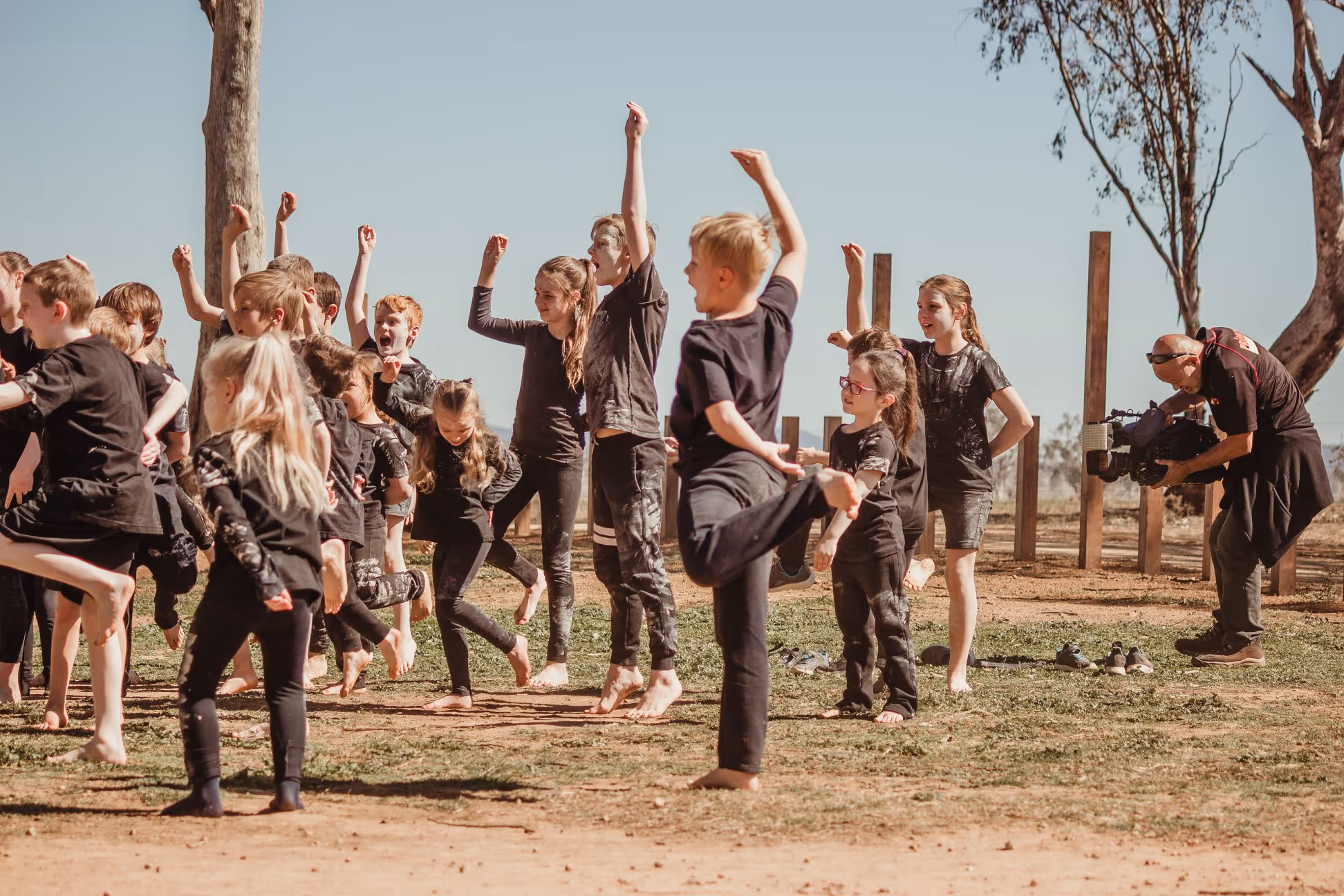 Group of children in black clothes performing outdoor cultural dance barefoot.