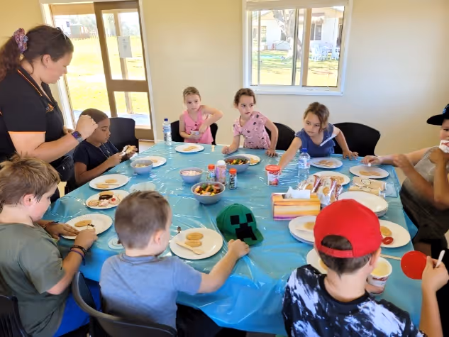 Children seated around a table with snacks and drinks in a bright room during a group activity.