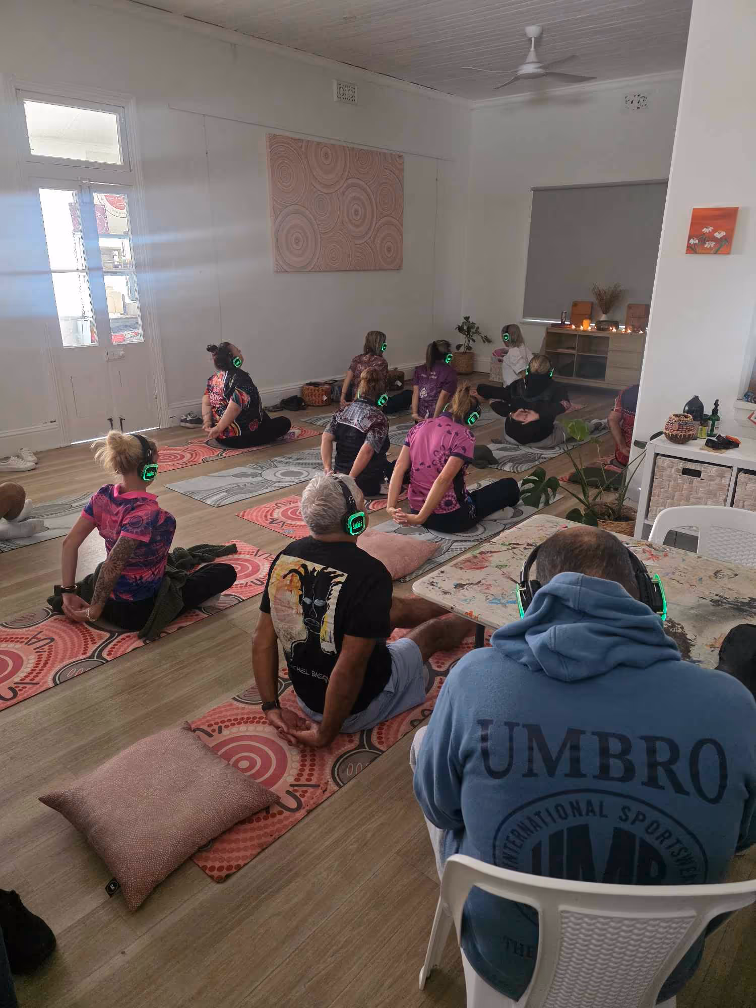 Group of people in a room doing yoga on mats wearing headphones .