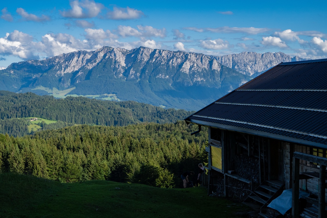 A house with a dark metal roof looking out over forested hills and a mountain range