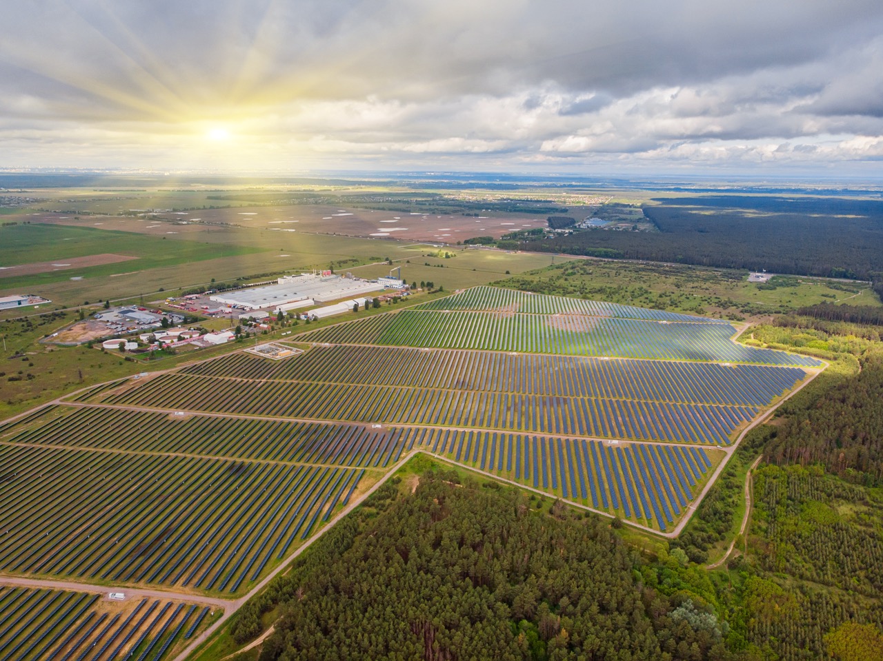 Aerial view of a large solar farm at sunrise, rows of panels laid out across farmland