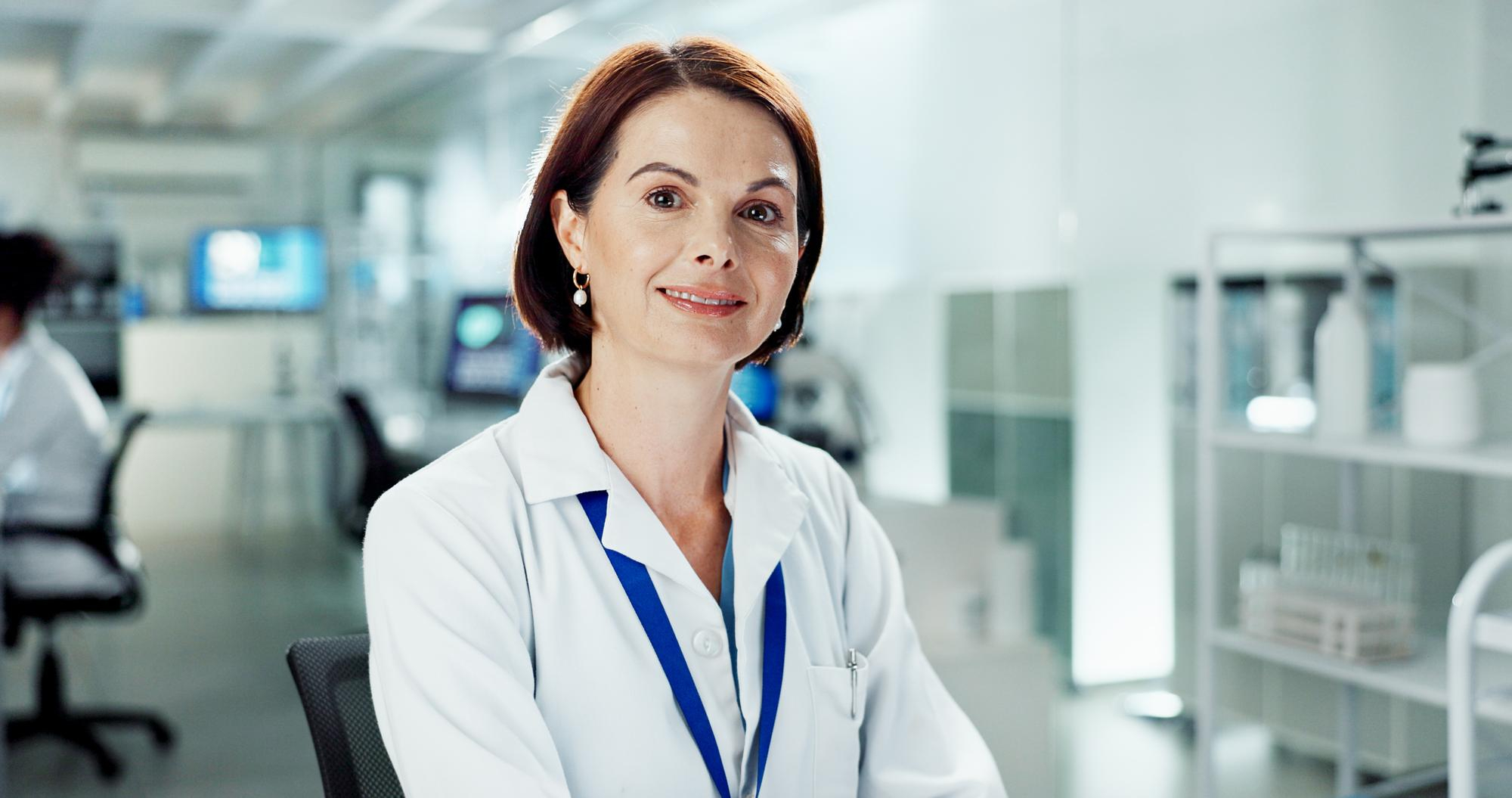 Female scientist wearing a white lab coat and blue lanyard in a laboratory setting.