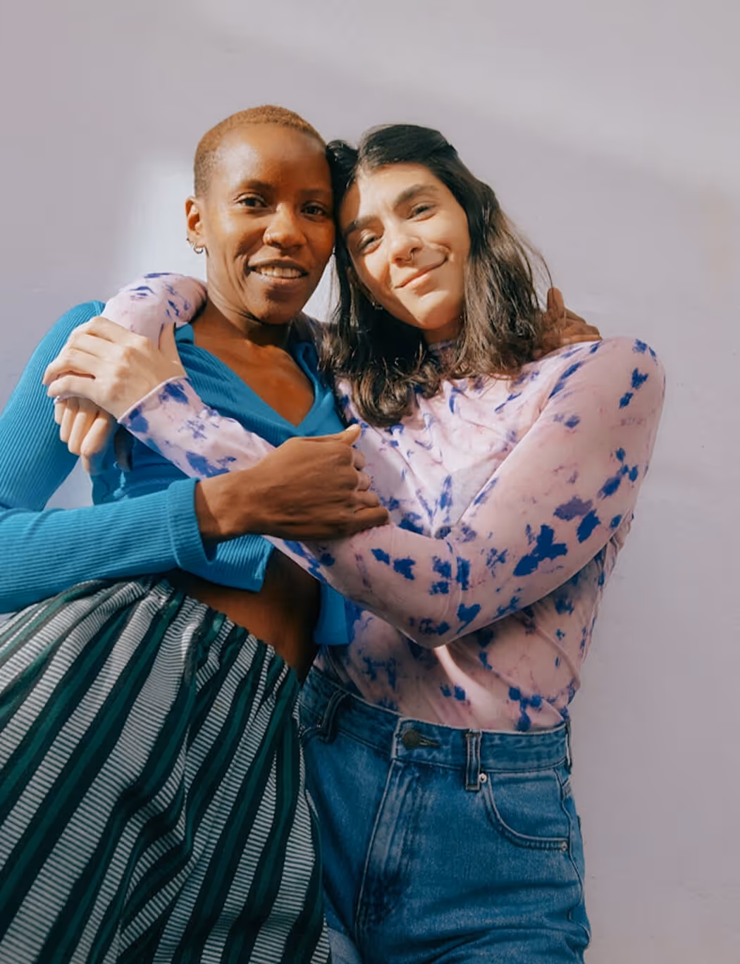 Two women wearing green recycling t-shirts holding a wooden crate filled with recyclable cans and containers.