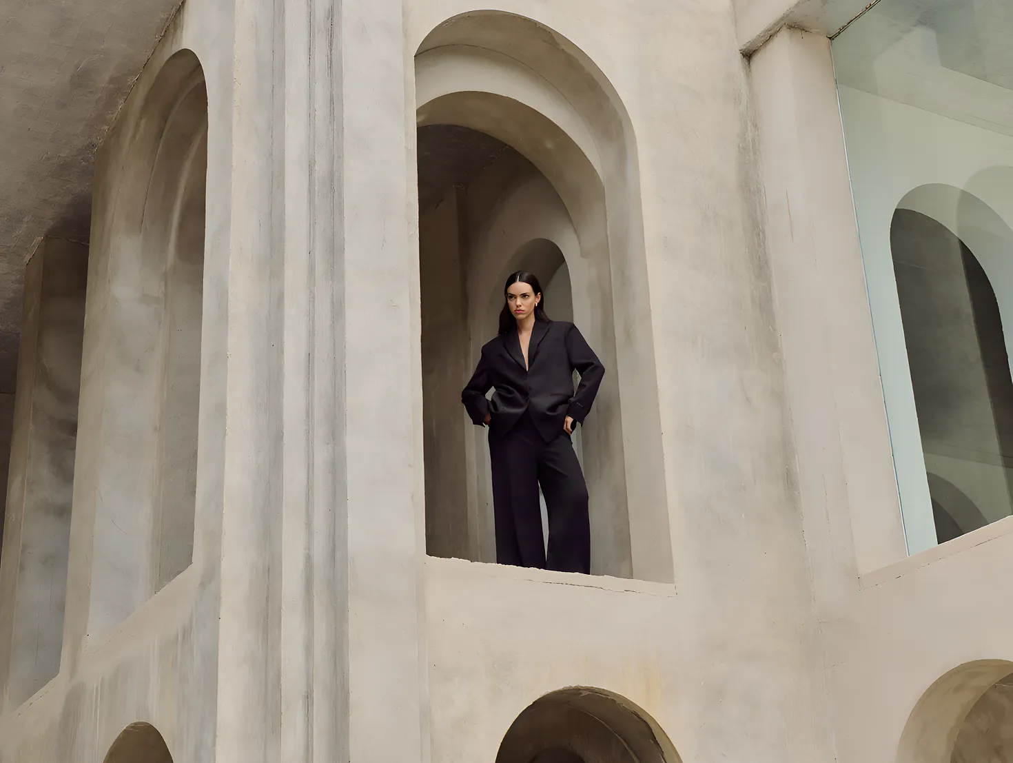 Woman in black suit standing in a large concrete archway with reflective glass nearby.