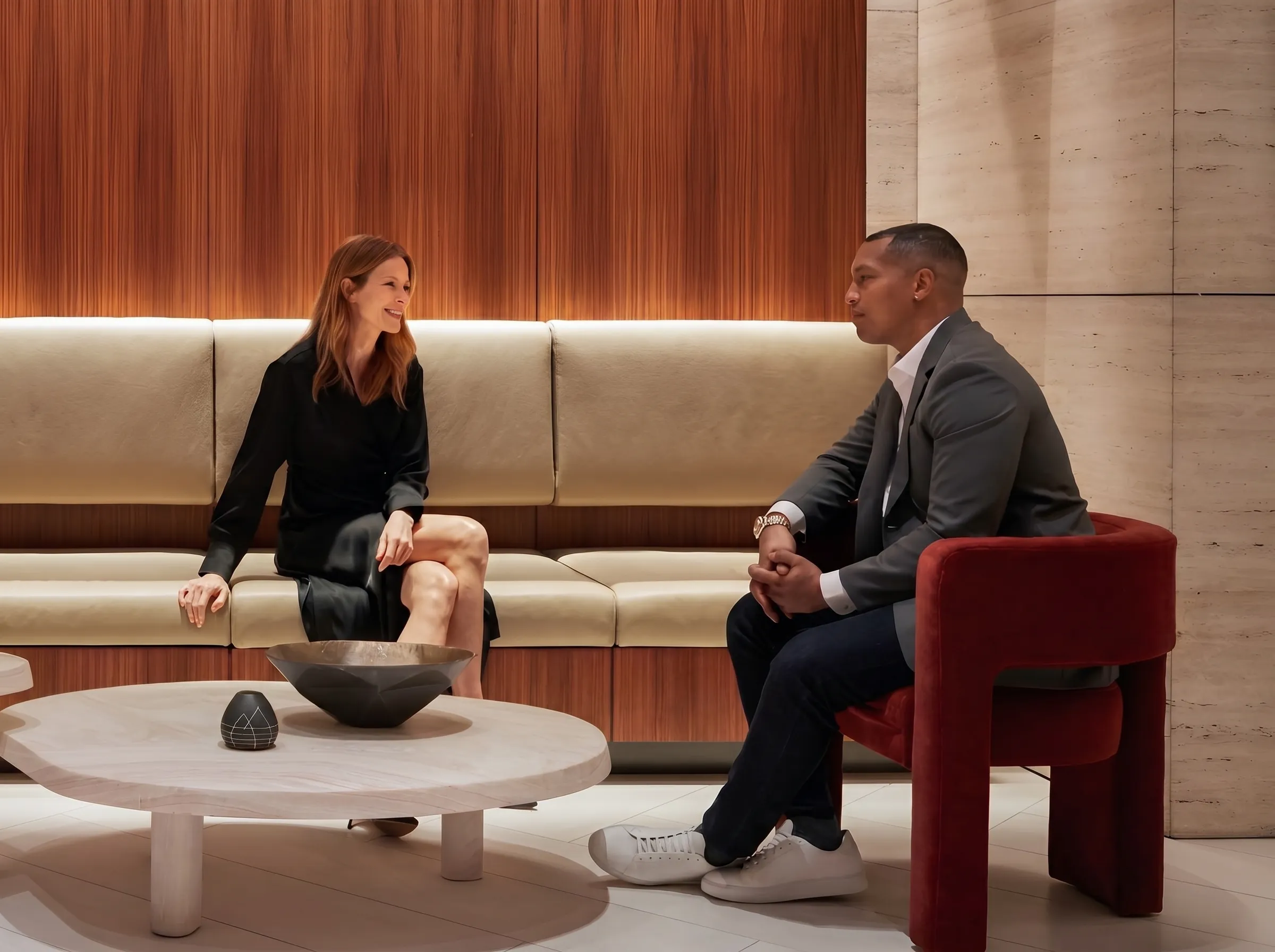 A man and woman sitting in a modern lounge having a conversation across a round table with decorative bowls.