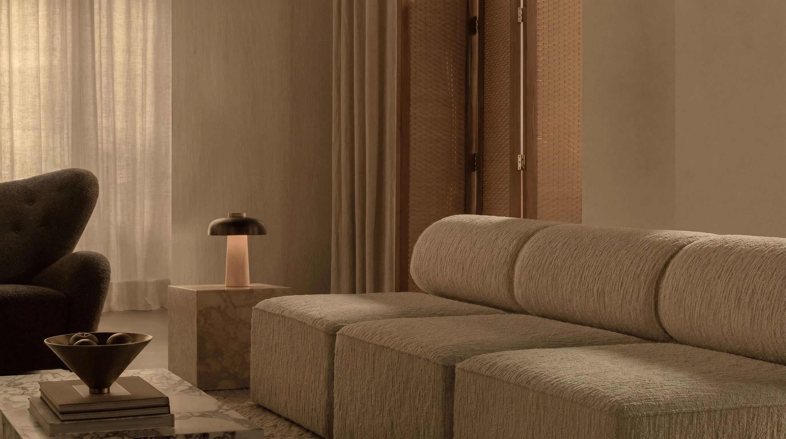 Neutral-toned living room with beige textured sofa, dark armchair, marble tables, and soft lighting.