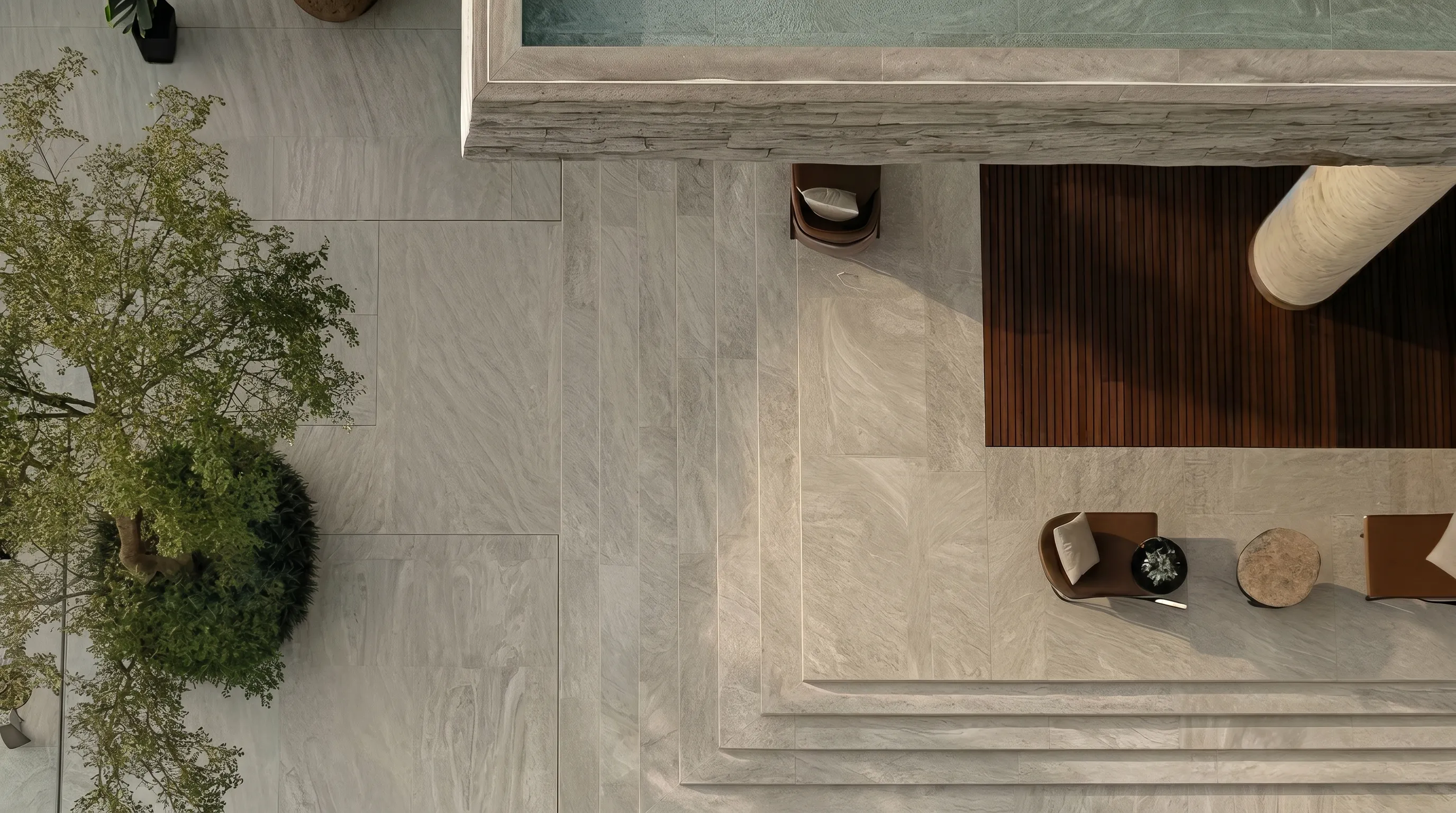 Top-down view of a modern outdoor patio with stone flooring, chairs, and a pool edge.
