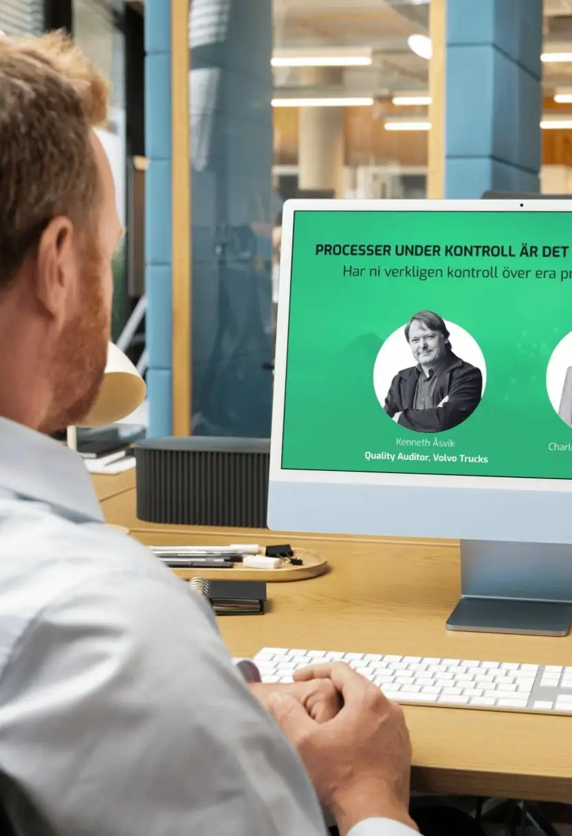 Man sitting at desk looking at computer screen displaying a presentation with text and a black-and-white portrait.
