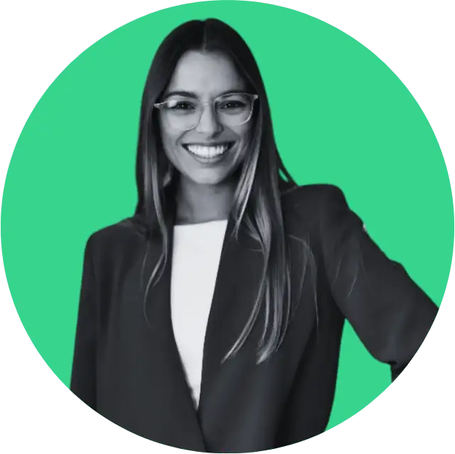 Smiling woman with long hair wearing glasses and a blazer against a green background.
