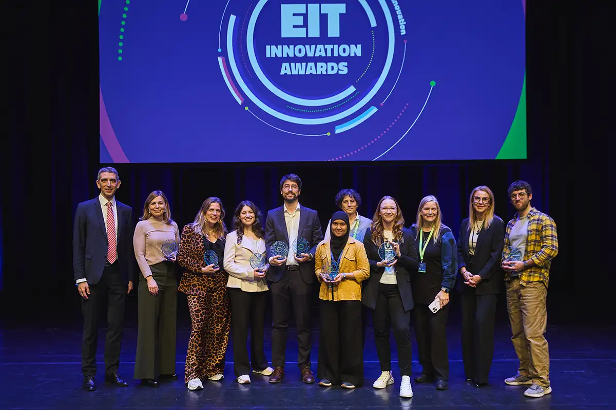 Group of 11 award winners posed on stage under EIT Innovation Awards banner, holding trophies.