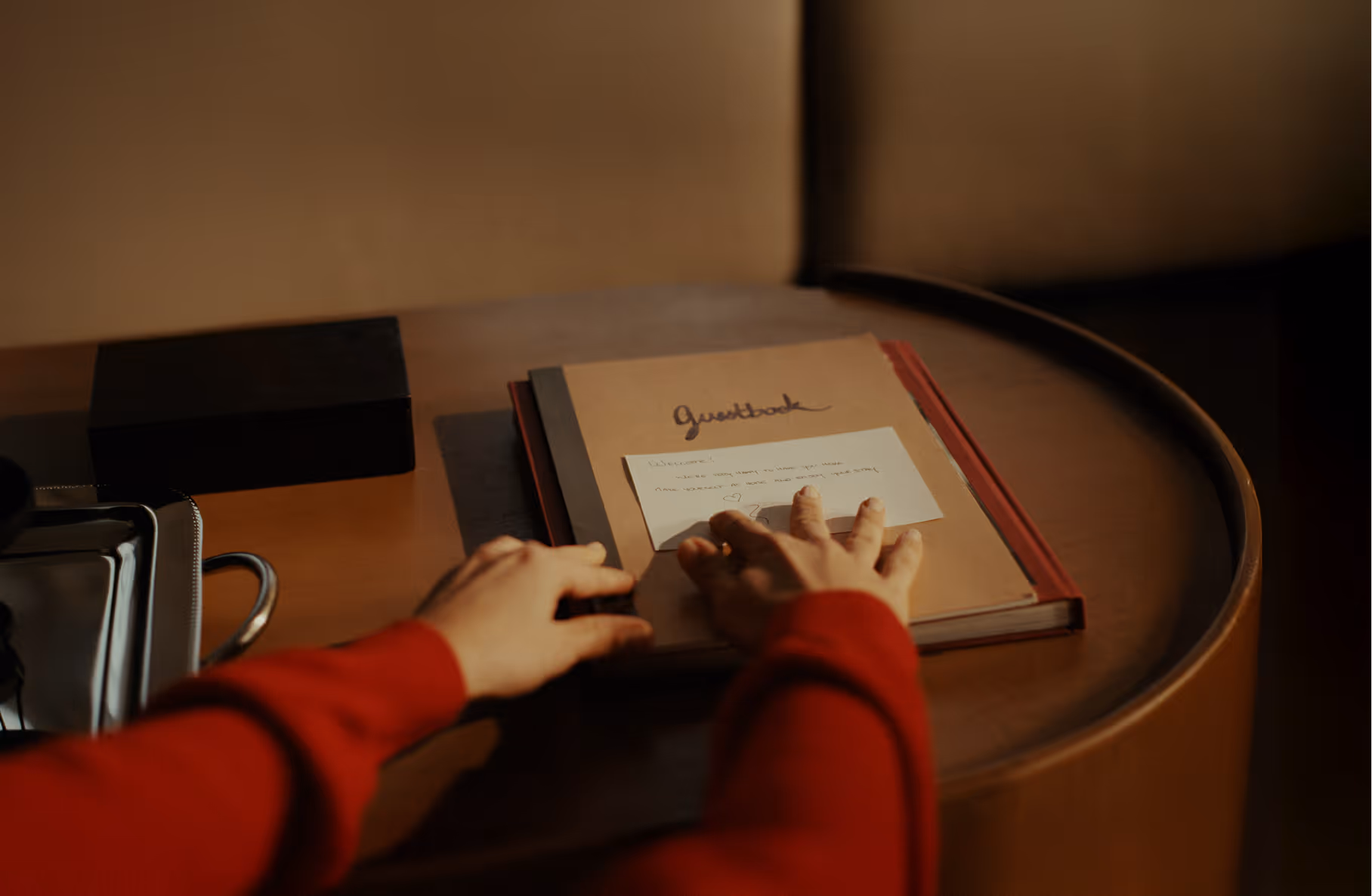 Person in red sweater placing a note on a guestbook on a round wooden table.