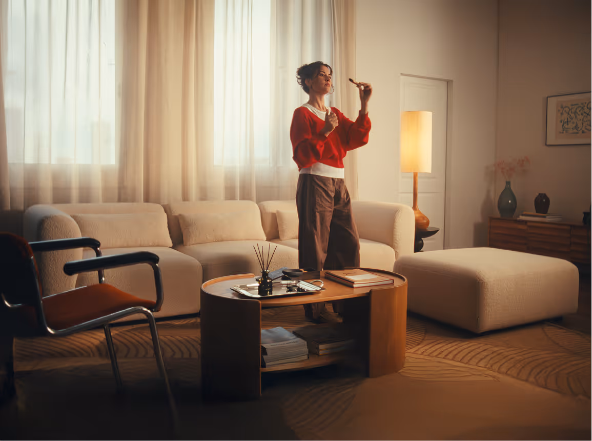 Woman in a red sweater standing in a cozy living room with beige sofa, wooden coffee table, and a floor lamp.