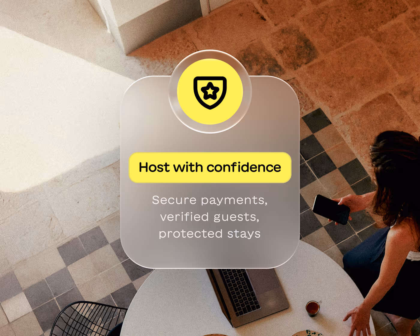 Graphic with shield icon and text 'Host with confidence' and 'Secure payments, verified guests, protected stays' over a top-down view of a woman holding a phone by a table with a laptop and cup.