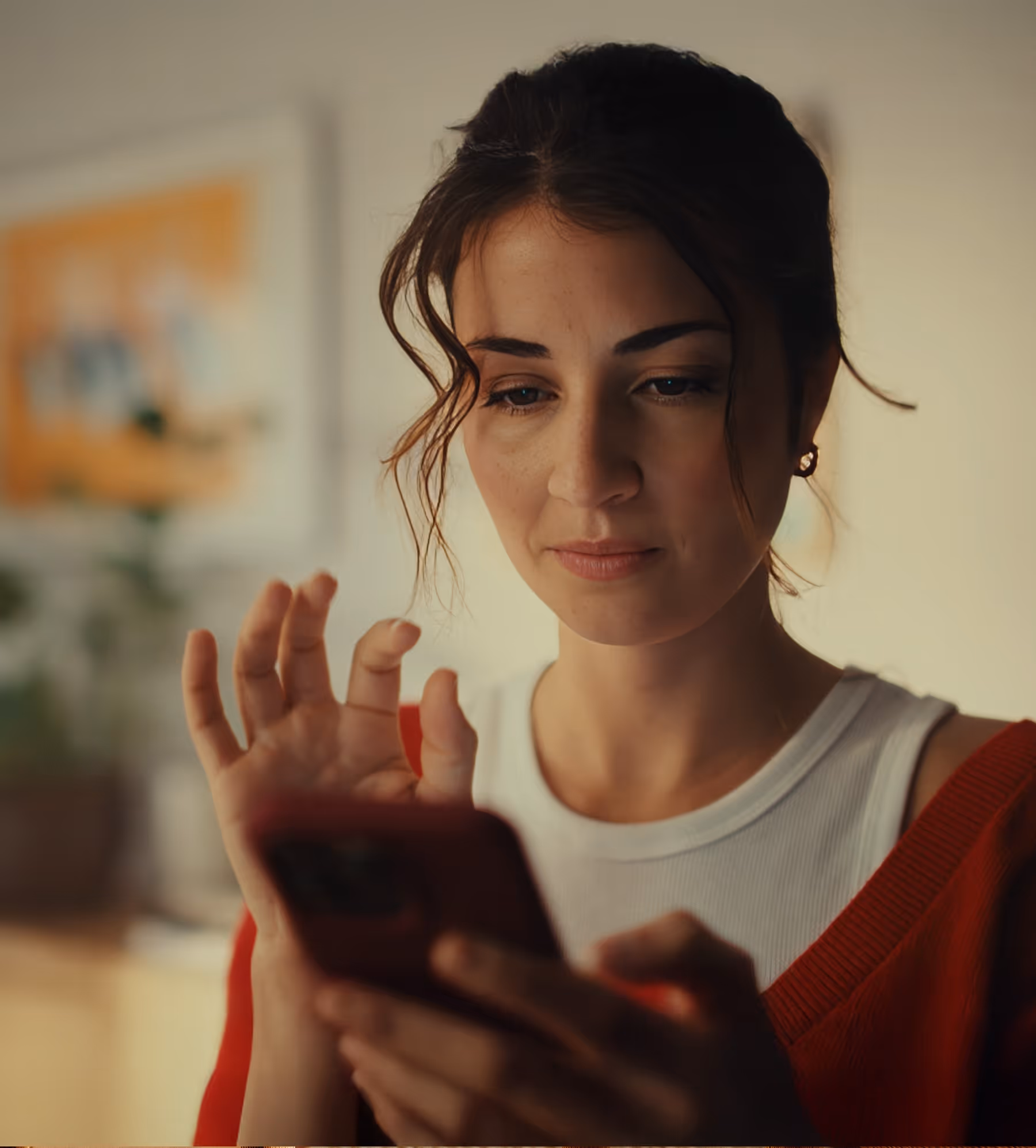 Young woman looking at her smartphone while making a gesture with her hand indoors.