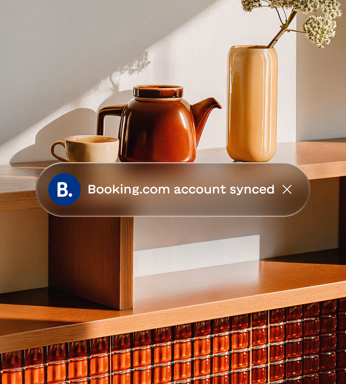 Wooden shelf with a brown ceramic teapot, beige cup, and tall beige vase with flowers under soft sunlight.