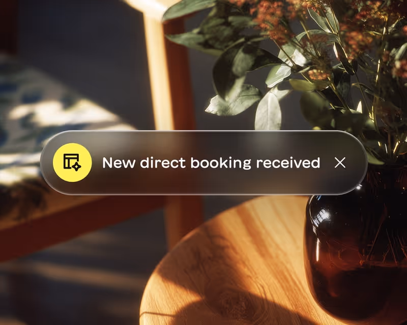 Notification message on screen stating 'New direct booking received' with a yellow icon and a close button, set against a background of a wooden table and a vase with flowers.