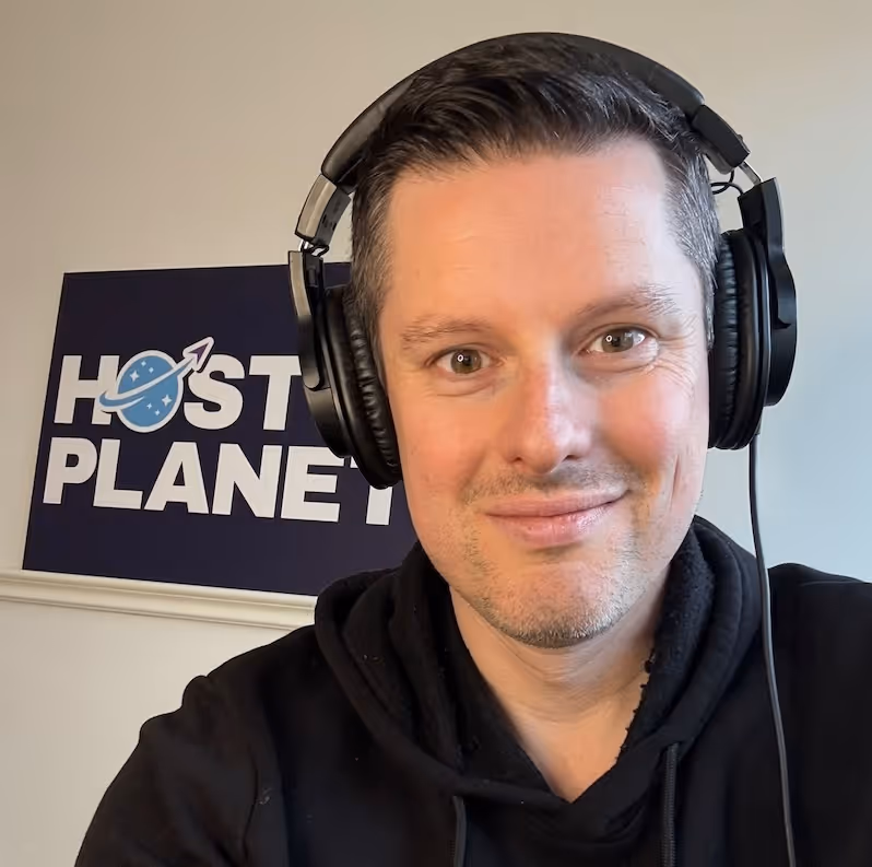 Man wearing headphones and a black hoodie smiling with a Host Planet sign in the background.