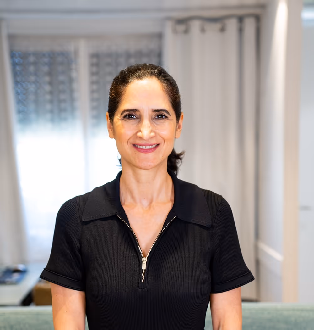 Femme souriante aux cheveux noirs attachés en arrière portant un haut zippé noir à l'intérieur.
