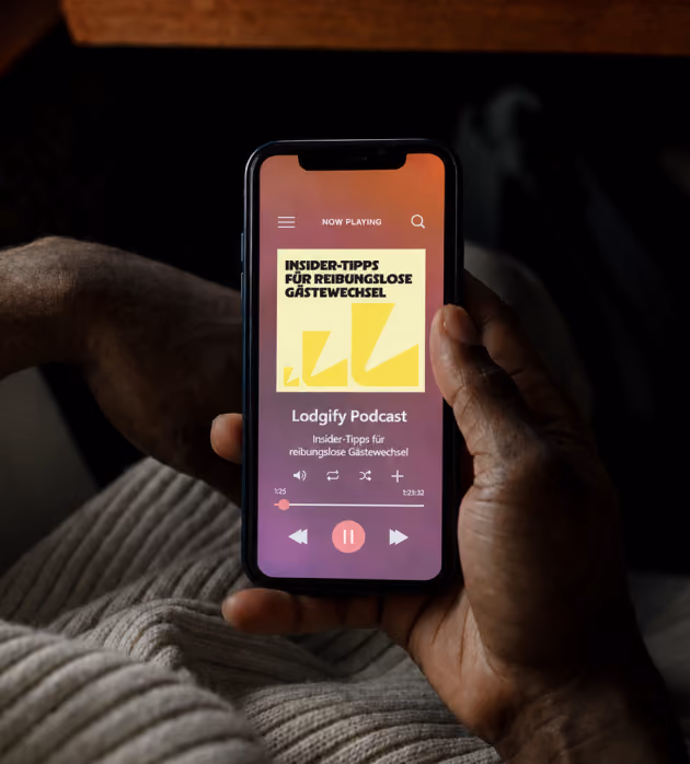 Handy in der Hand, auf dem der Lodgify Podcast mit Insidertipps für reibungslose Gastübergänge auf Deutsch abgespielt wird.