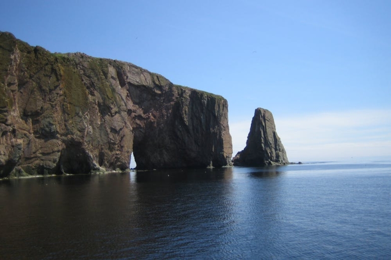 Large rugged rock formations rising from calm ocean water under a clear blue sky.