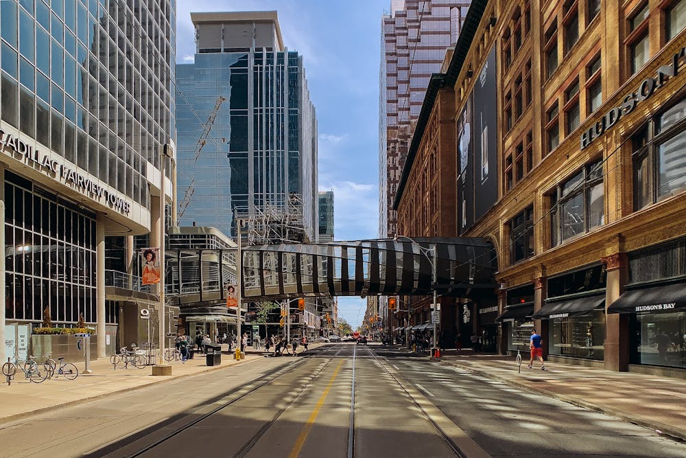 City street with elevated glass walkway connecting buildings, including Cadillac Fairview Tower and Hudson