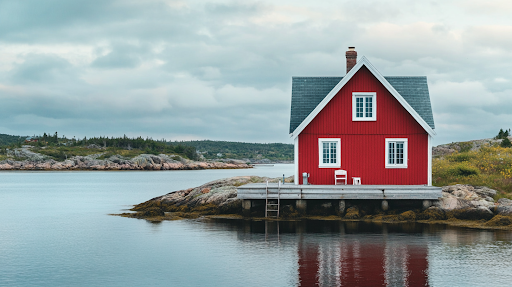 Red house on a wooden dock over calm water with rocky shore and cloudy sky in the background.