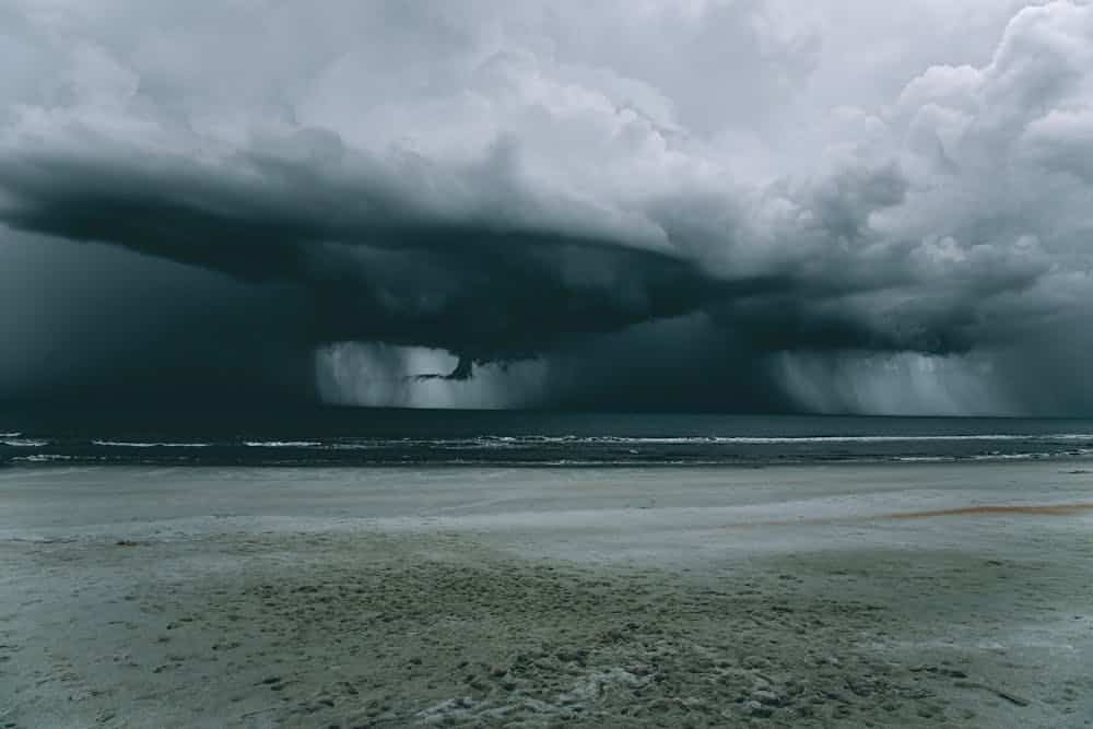 Dark storm clouds over ocean with heavy rain and a beach in the foreground.