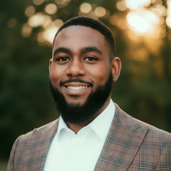 Smiling bearded man wearing a plaid suit jacket with a white shirt against a blurred background.