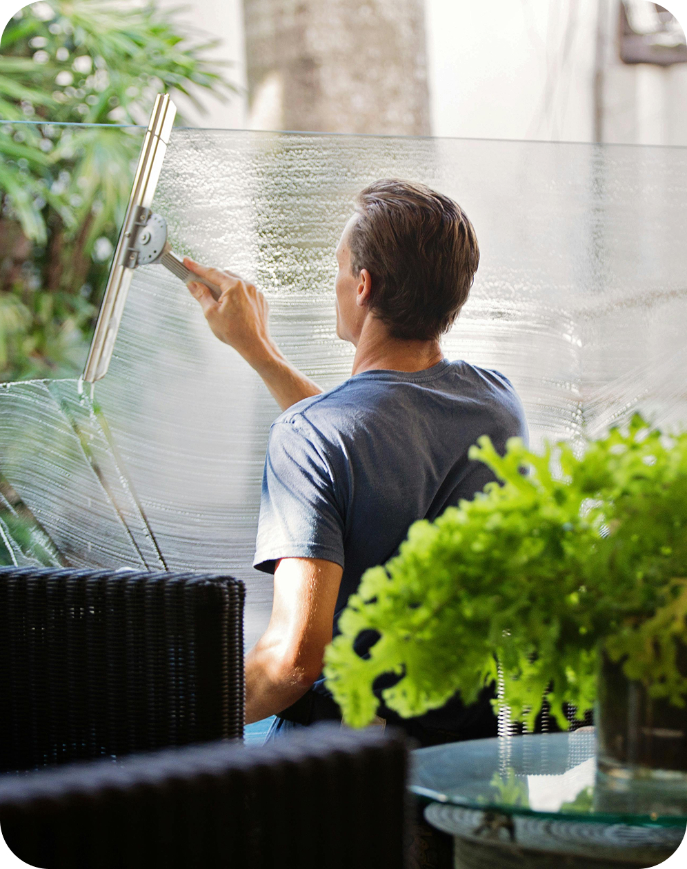 A professional window cleaner using a squeegee to clean a large glass office pane or balcony divider.