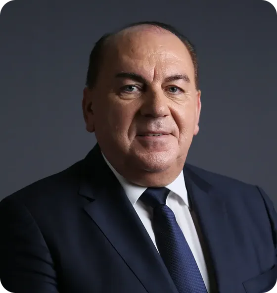 Middle-aged man wearing a dark suit, white shirt, and dark tie, posing against a dark gray background.