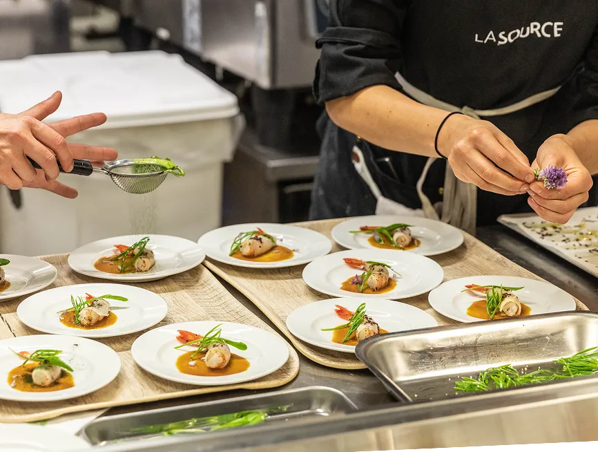 Chefs garnishing plates with herbs and flowers in a professional kitchen setting.