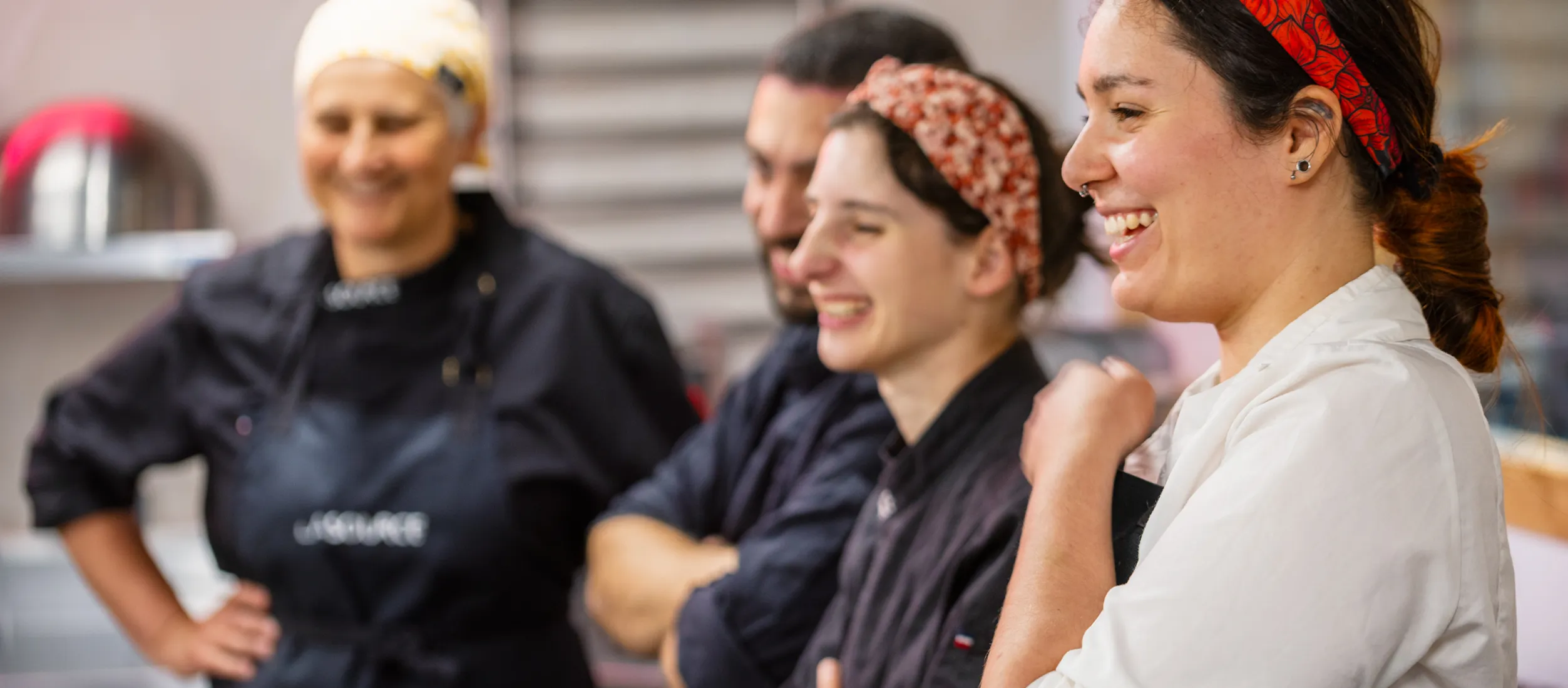 Quatre personnes souriantes en tenue de cuisine se tiennent côte à côte en cuisine.