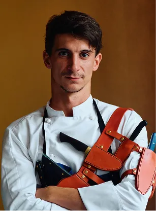 Jeune chef cuisinier portant une veste blanche et un tablier en cuir avec des couteaux. Crédit photo : Laurent Hazgui