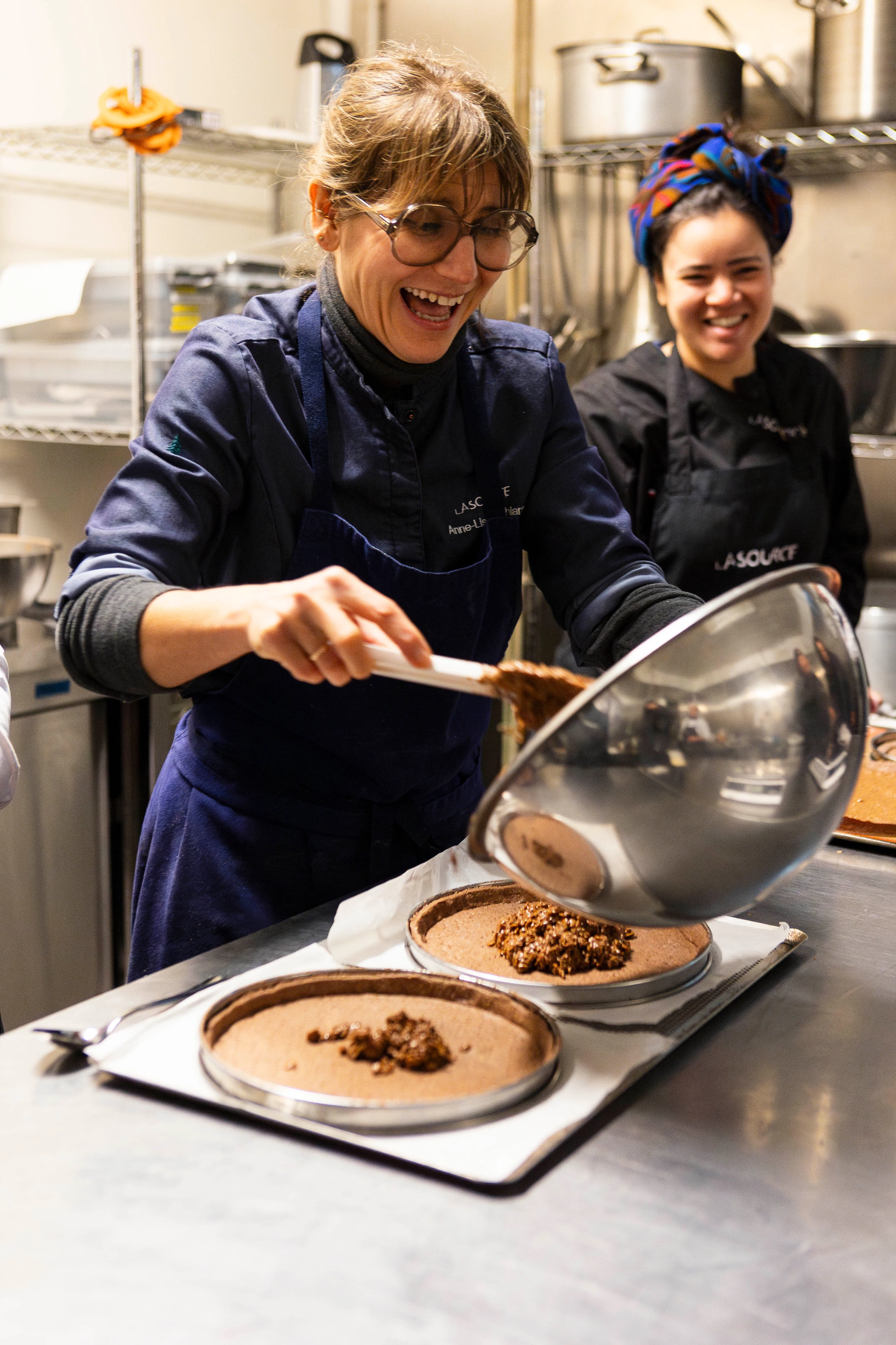Une pâtissière en tablier blanc prépare des ingrédients dans un plan de travail en cuisine.